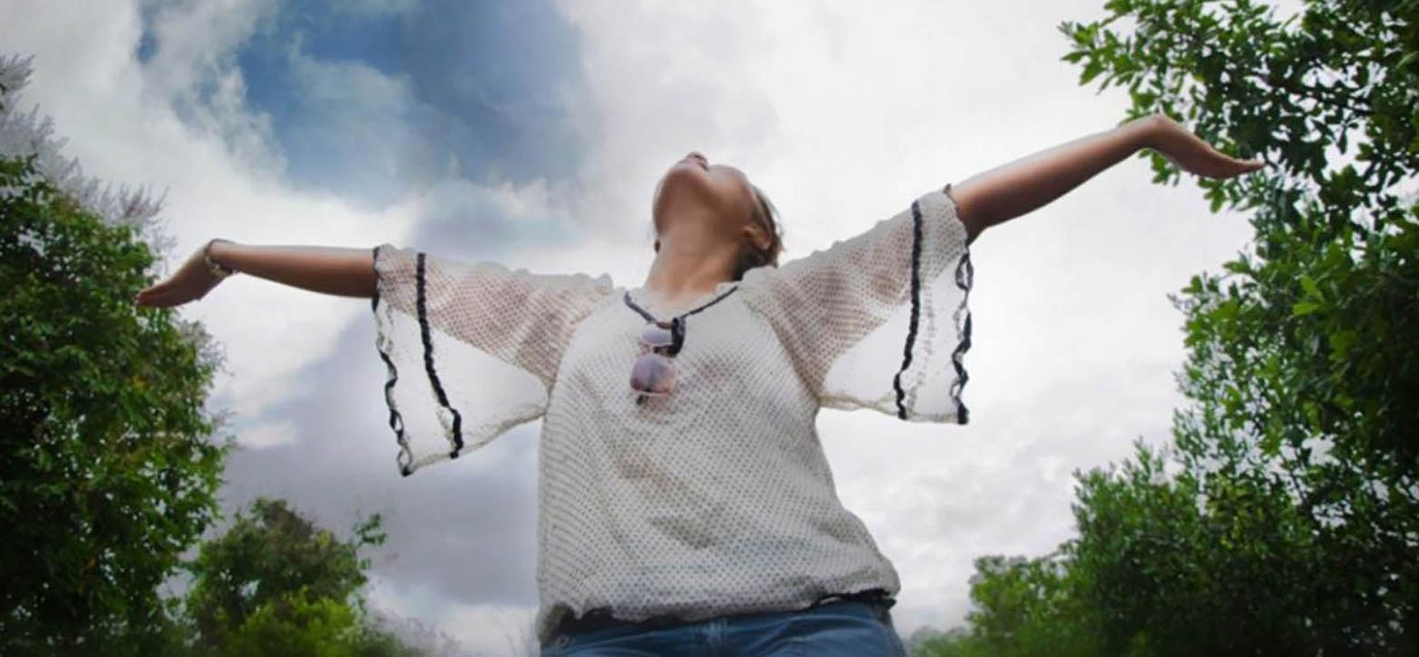 A student at Latham Centers enjoys the sun on a summer day, arms outstretched to the sky.